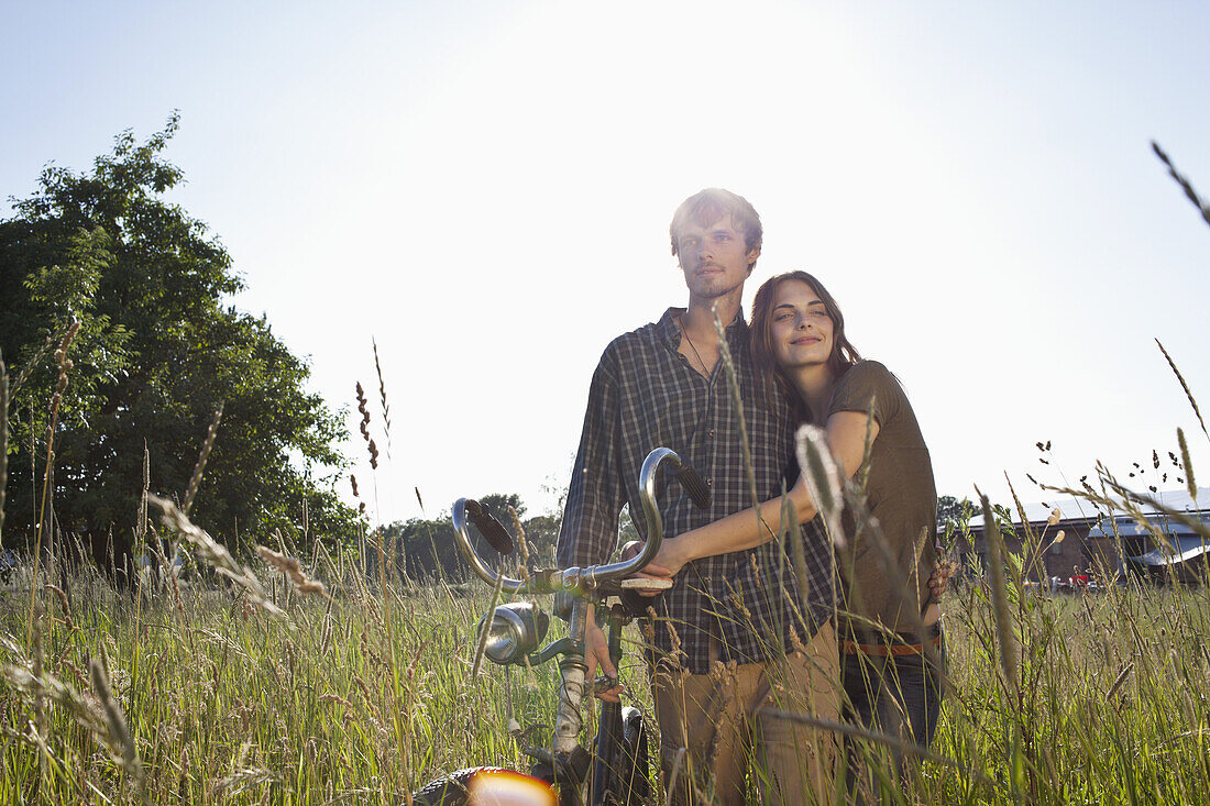 Couple with arms around each other walk through field with bike