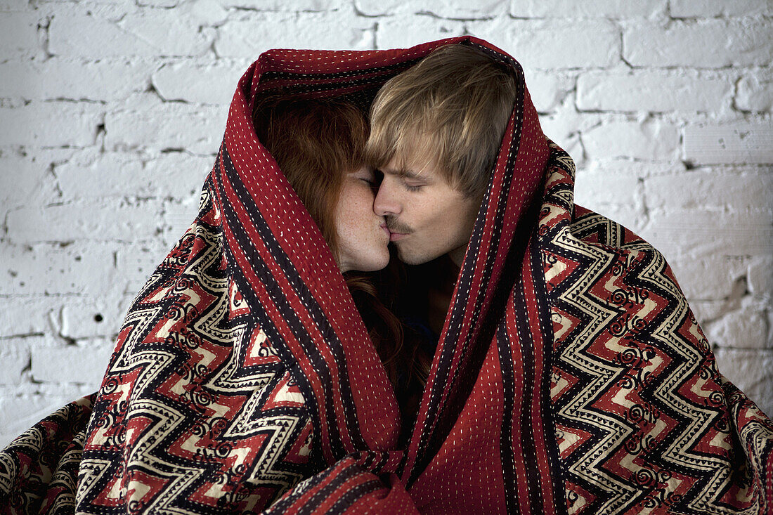 A young couple wrapped in a blanket kissing