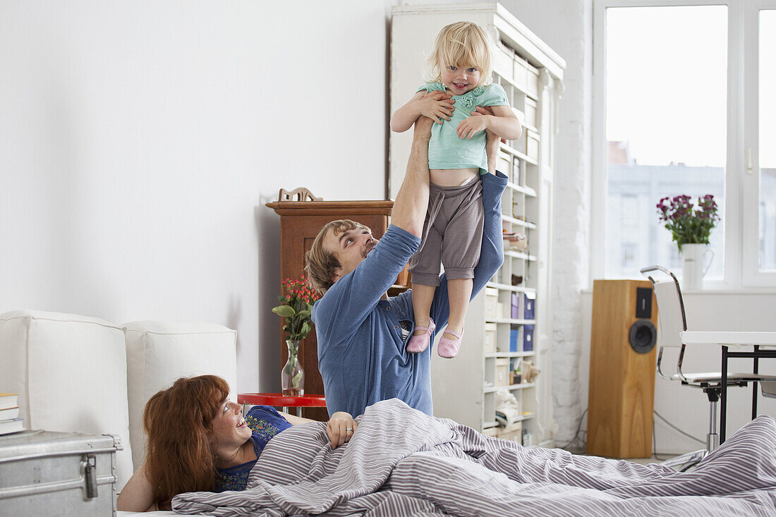 A couple in bed, man holding daughter aloft