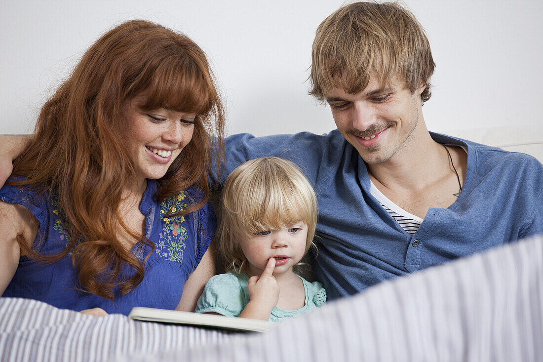 A young family reading a picture book in bed