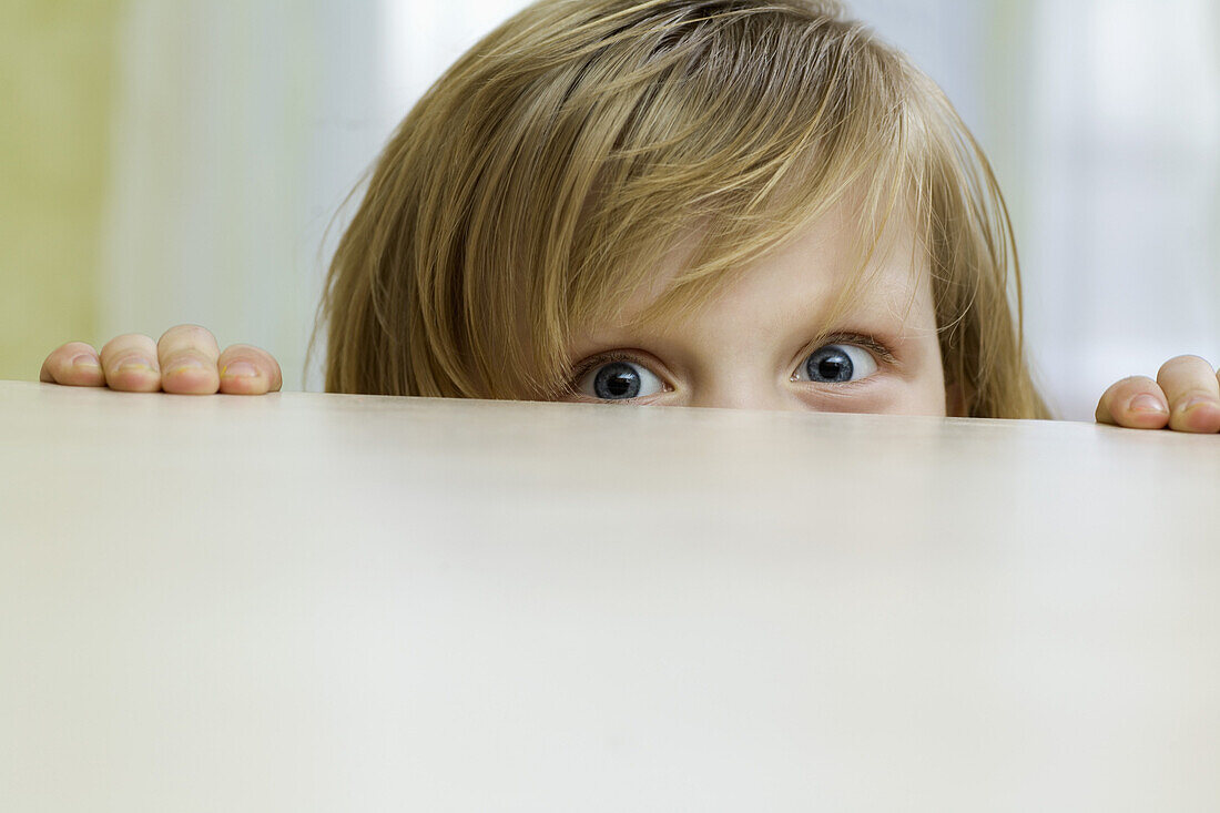 A mischievous girl peeking over the top of a table