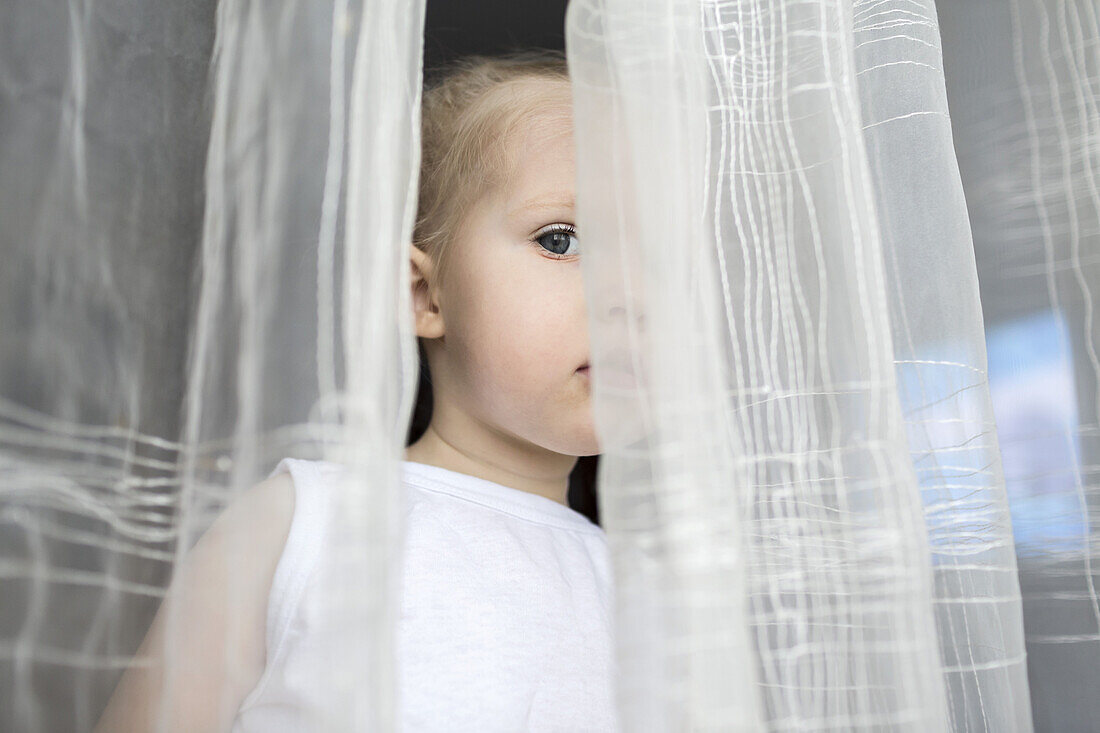 Girl peeking between translucent curtains