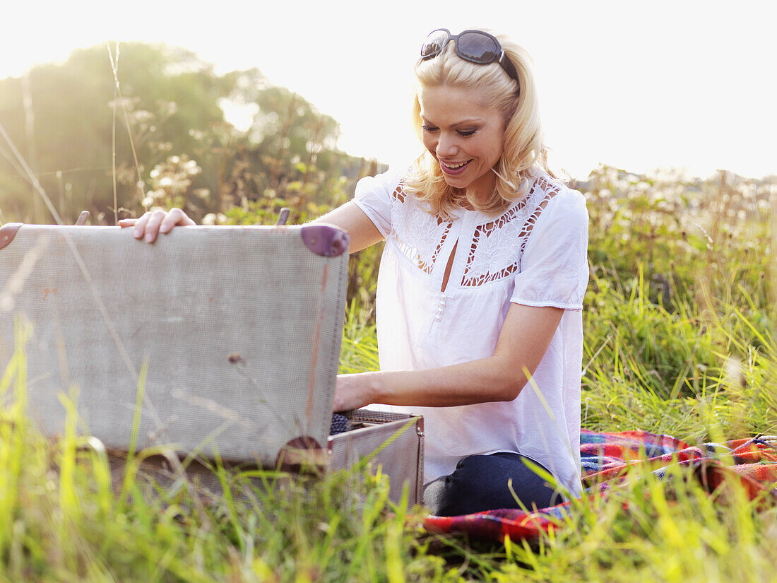 A woman sitting in the grass rummaging through an open suitcase