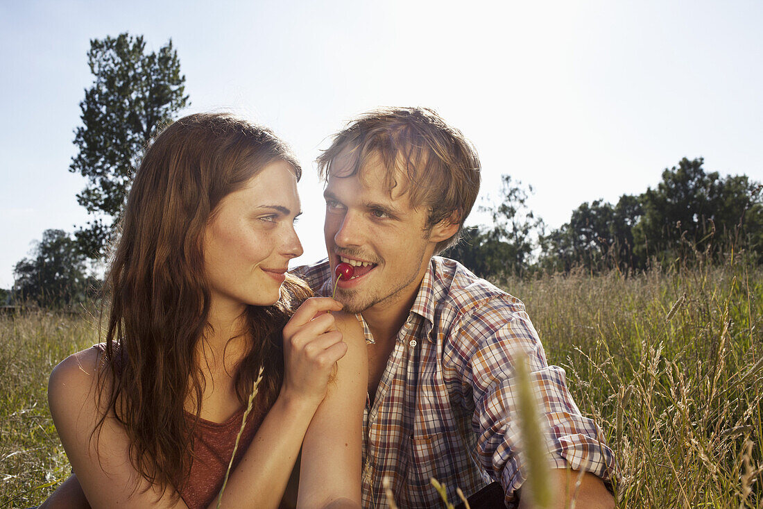 Girlfriend feeds her boyfriend a cheery amongst the timothy grass