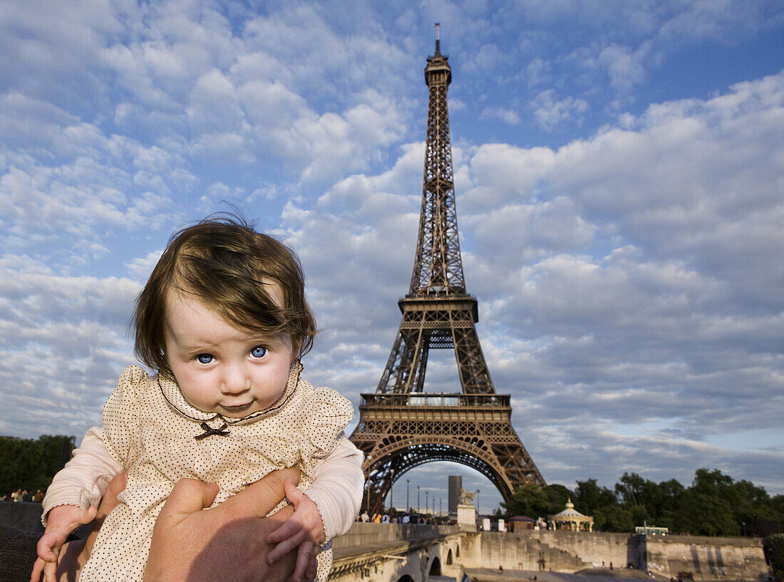 A baby being held aloft in front of the Eiffel Tower, Paris, France