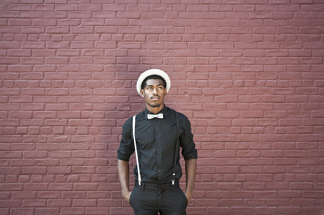 A young black man dressed in bow tie, suspenders and hat