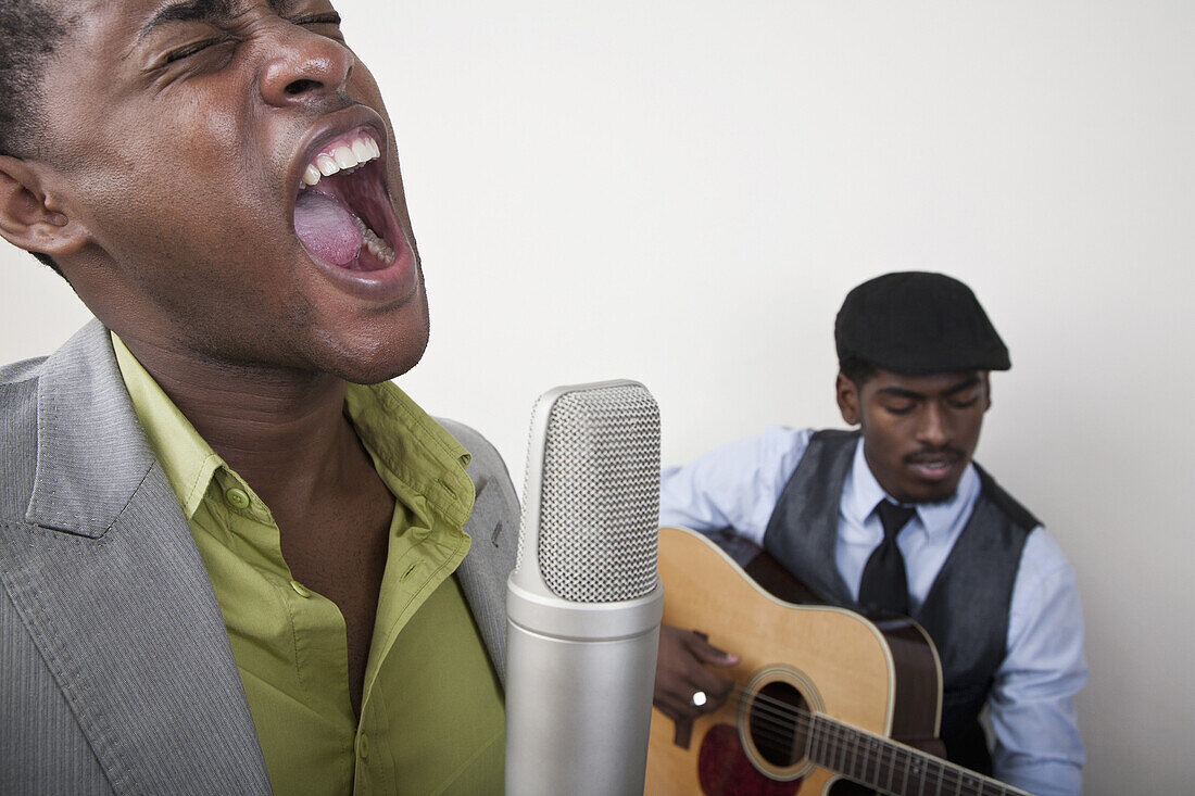 A man singing with a retro microphone, guitarist in background