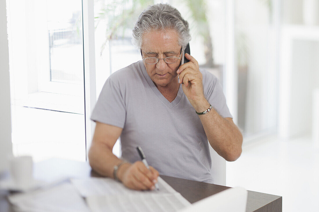 A senior man using the phone and writing on a document