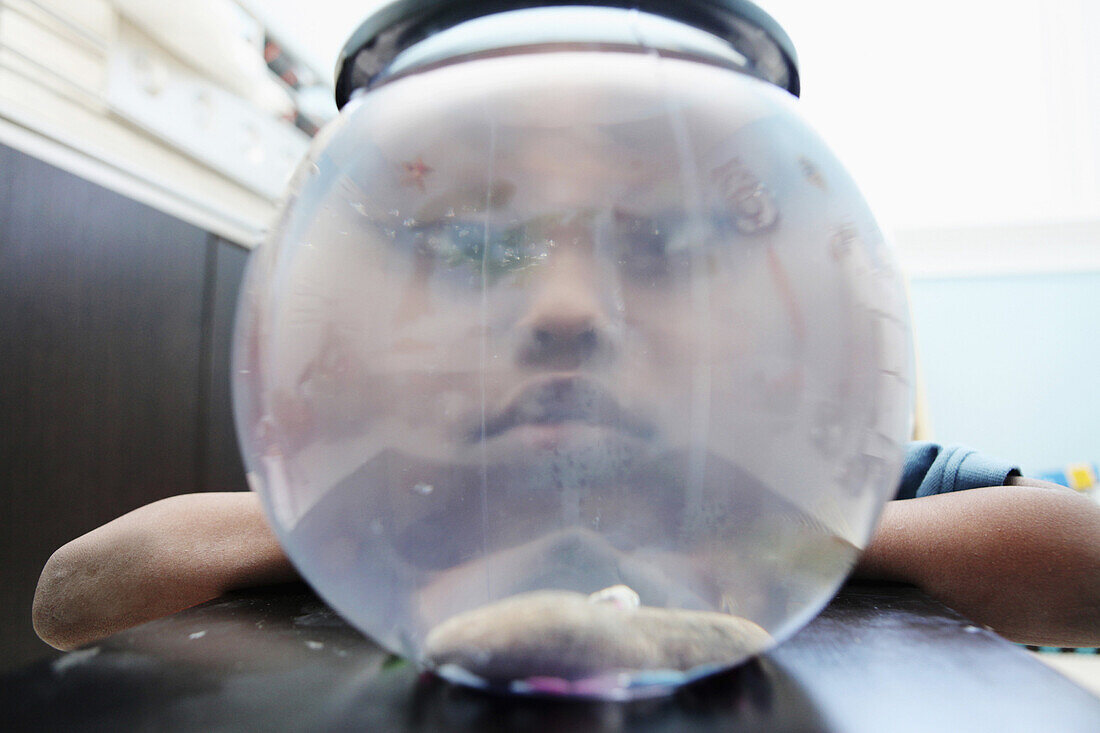 A frowning boy looking through a fishbowl with no fish