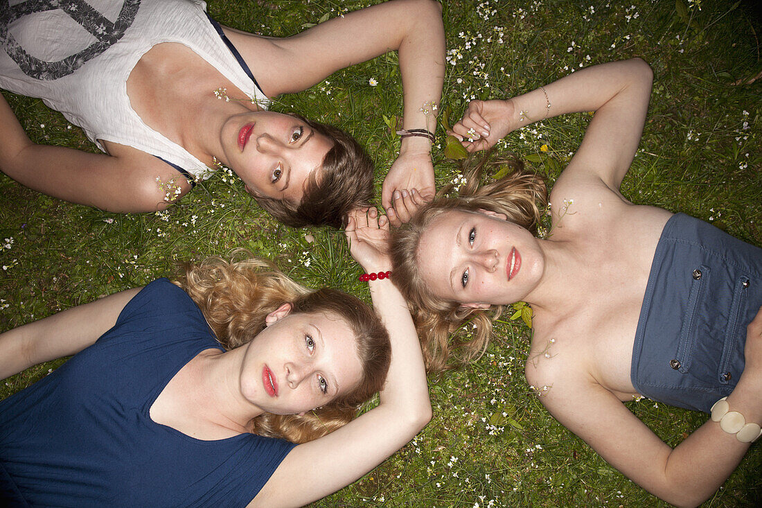 Three female friends lying in the grass in a circle looking sensually at the camera