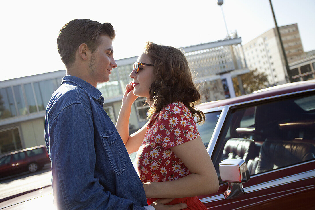 A rockabilly couple standing face to face next to a vintage car