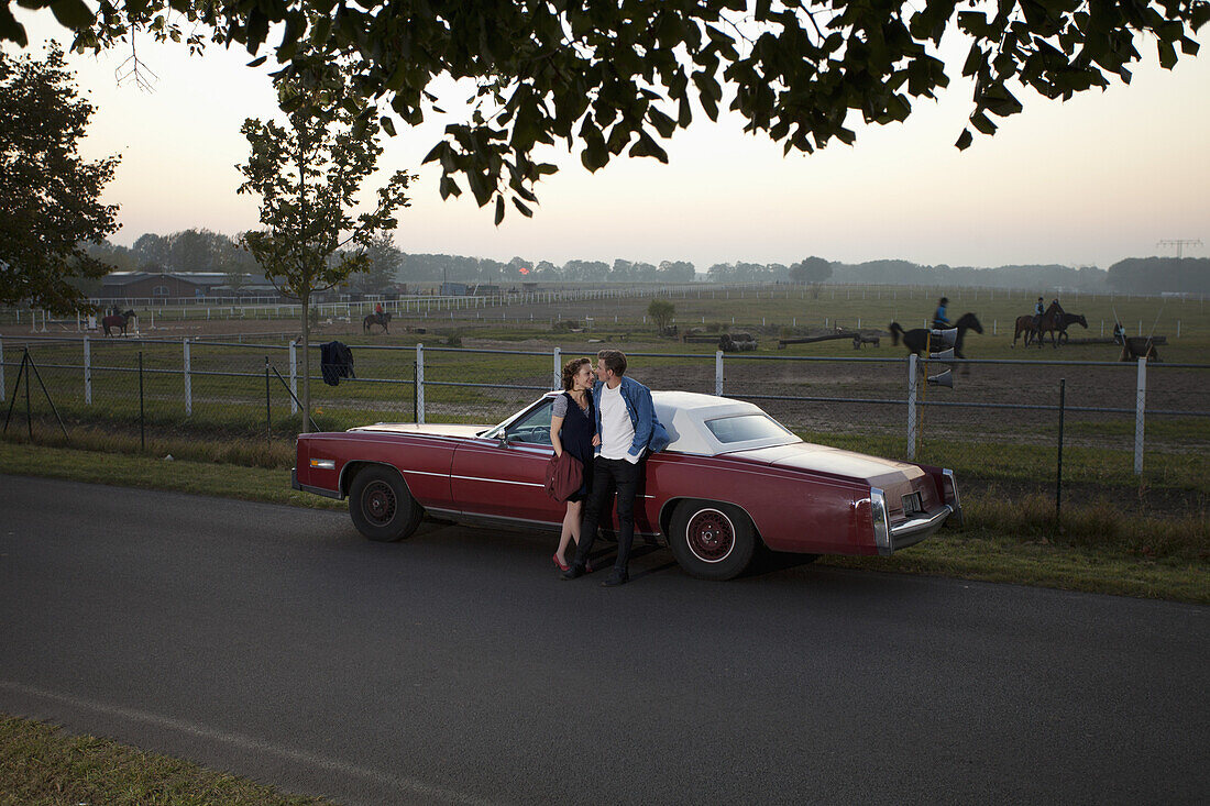 A rockabilly couple leaning against a vintage car in the country