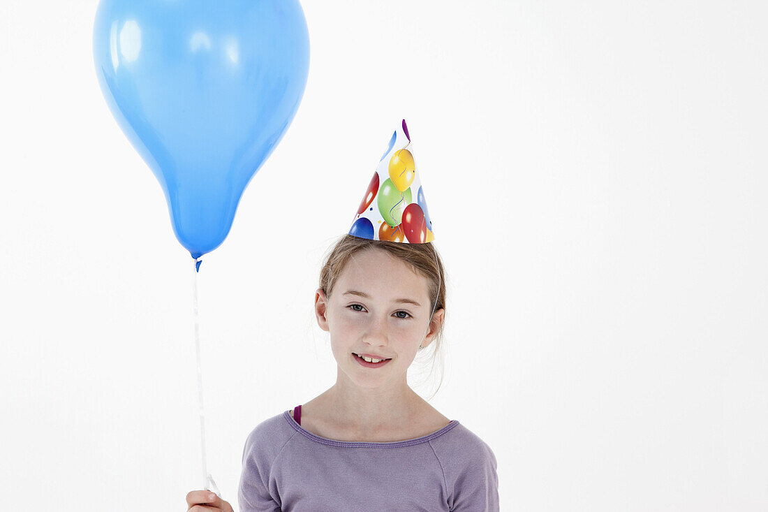 A girl wearing a party hat and holding a balloon, close-up