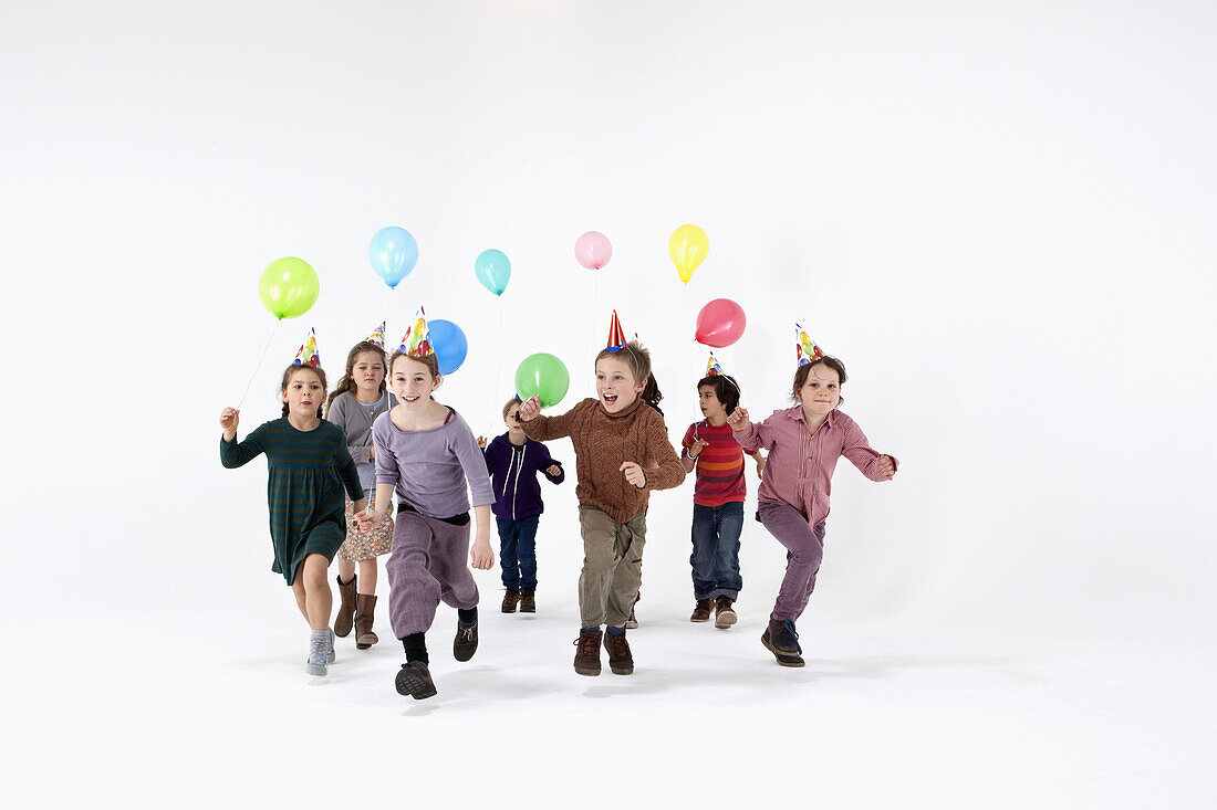 A group of kids in party hats and carrying balloons running forward