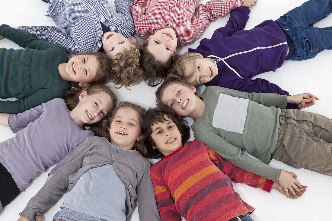 A group of kids lying on their backs in a circle, heads touching