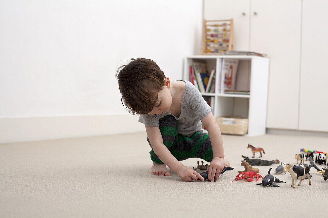 A little boy playing with some toy animal figurines on the floor of his bedroom