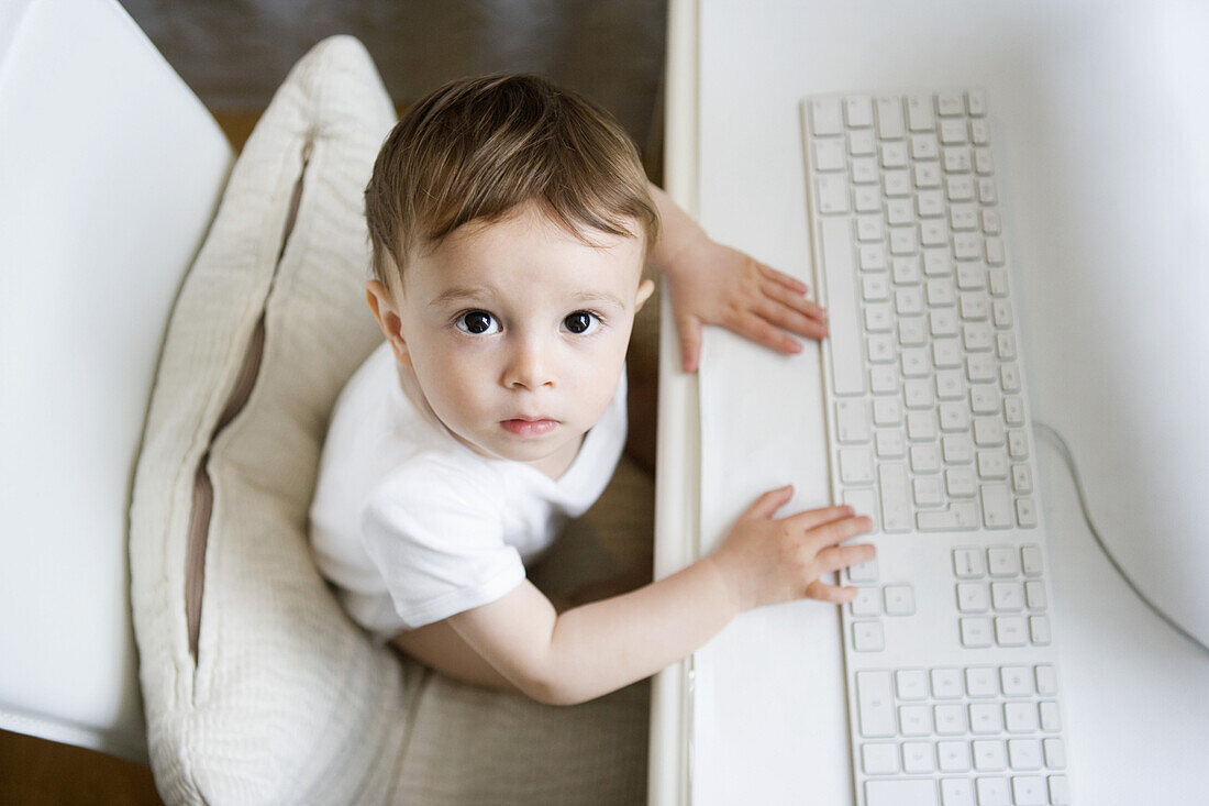 A toddler sitting at a desk with a computer keyboard