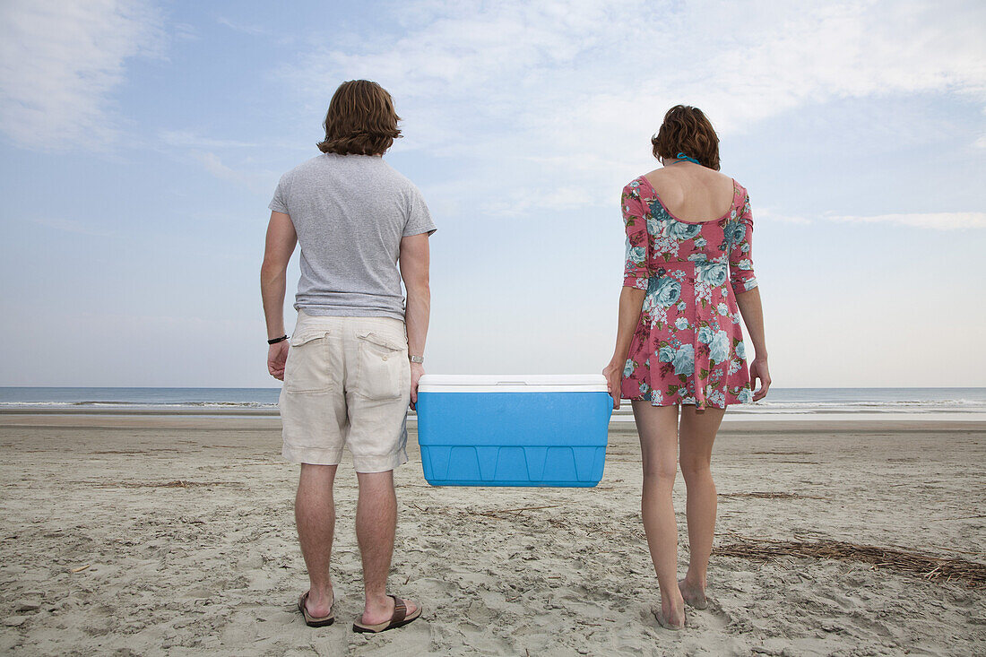 A young couple carrying a cooler together on the beach