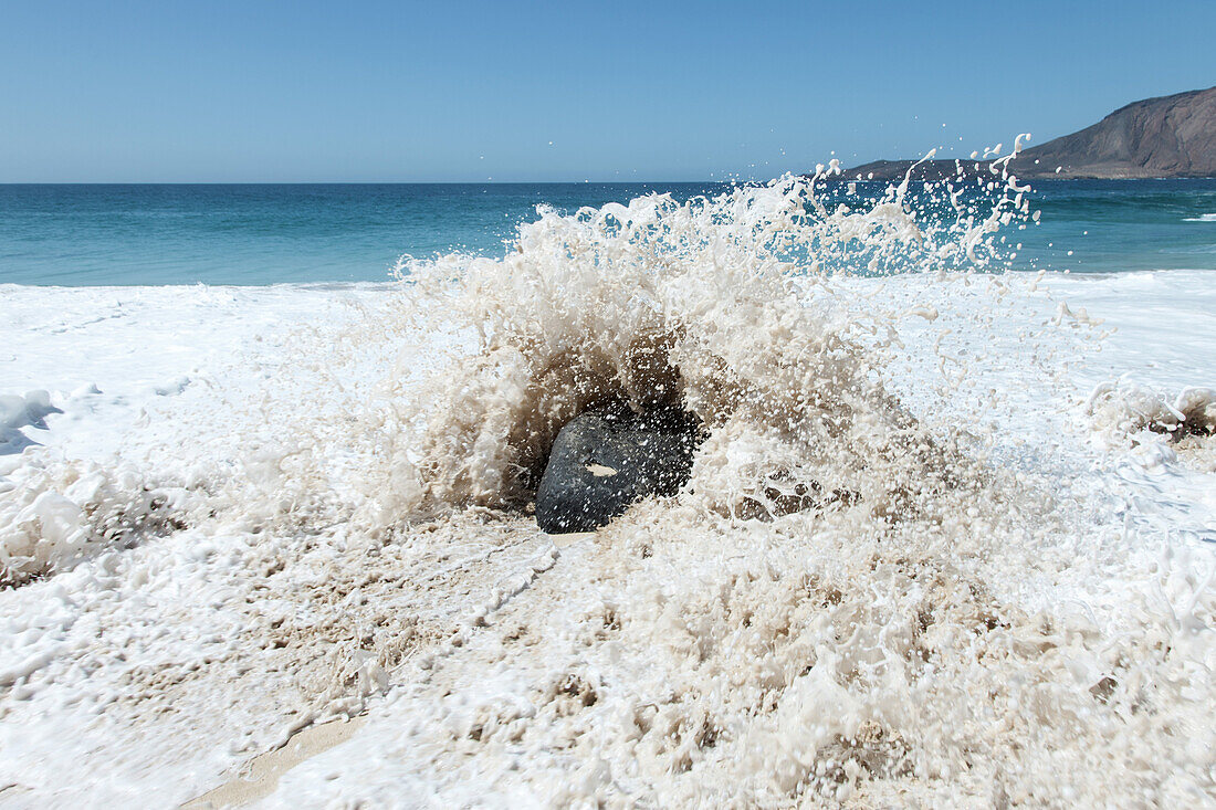 Splash of wave against rock on beach in La Graciosa, Canary Islands, Spain