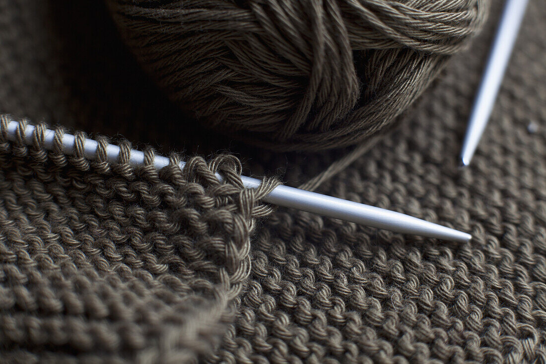 A pair of knitting needles, knitting and a ball of yarn, full frame