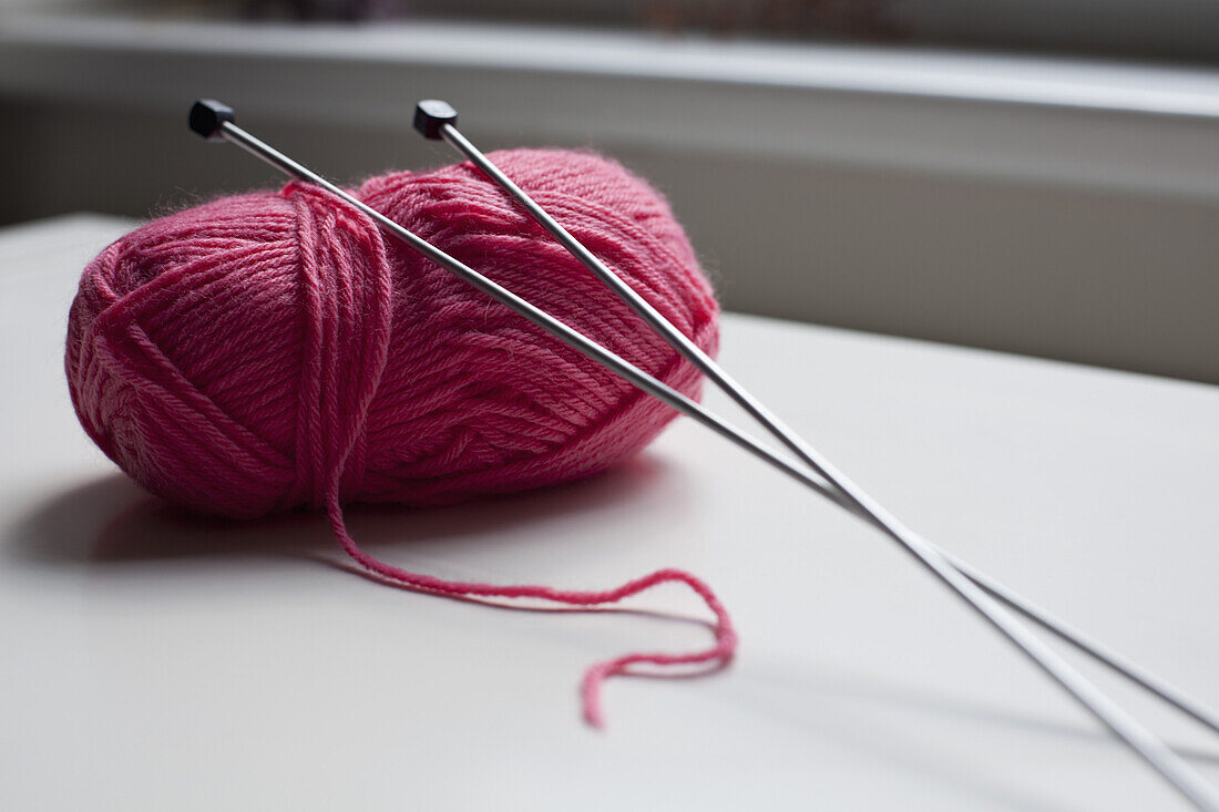 A ball of yarn with a pair of knitting needles leaning on it