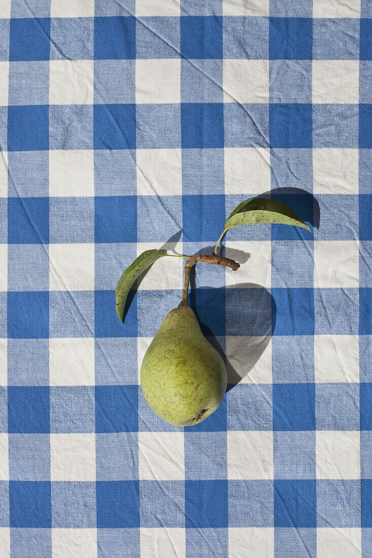 A single freshly picked pear on a checked tablecloth