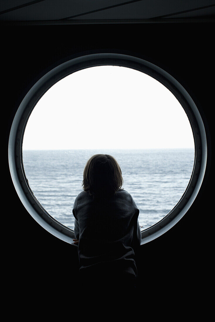 Rear view of a boy looking through a porthole