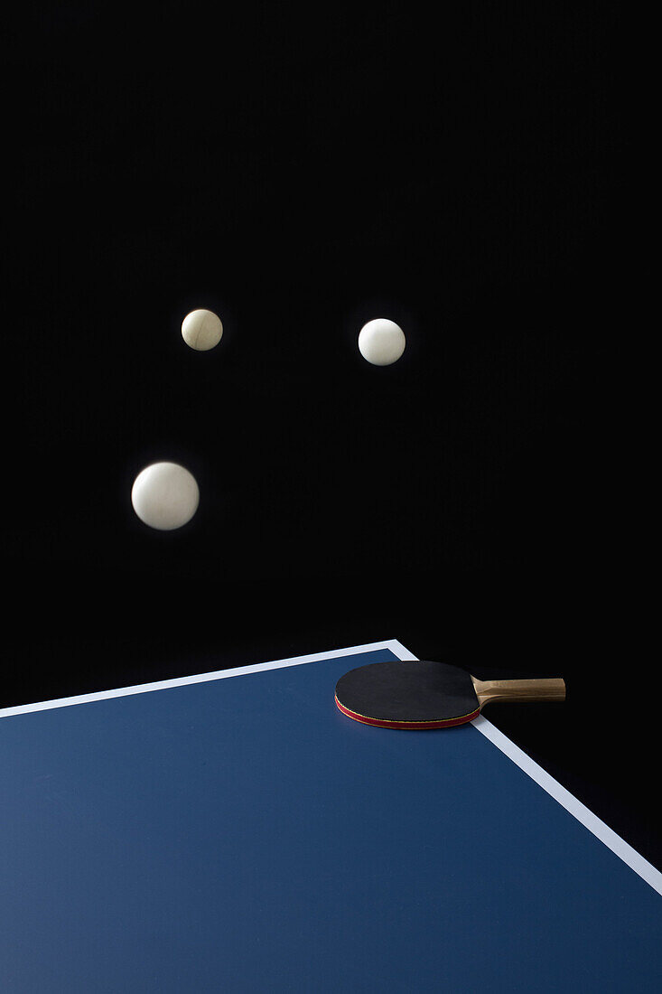 Table tennis balls mid-air and a bat on a table