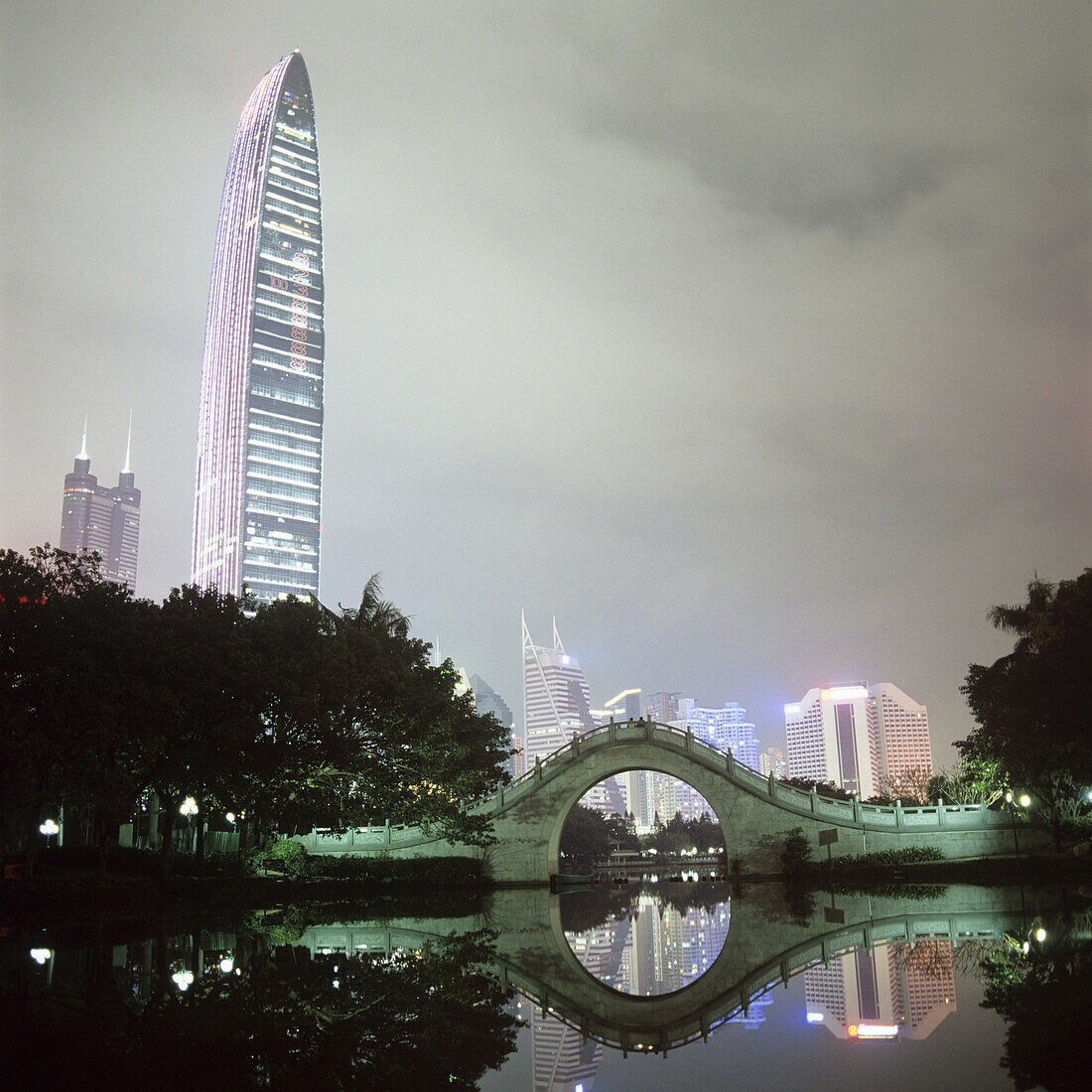View of illuminated city buildings across water at night, Shenzhen, China