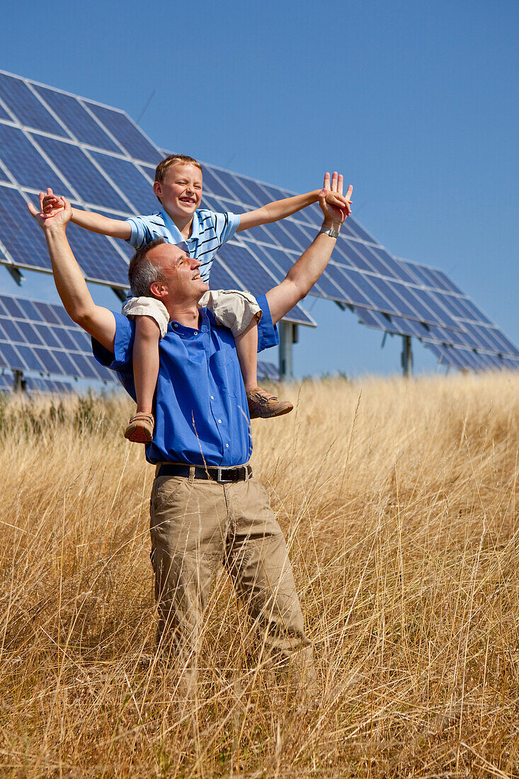 Solar park in summer, man carrying his son on his shoulders and are delighted by the sun, Lieschensruh, Edertal, Hesse, Germany, Europe