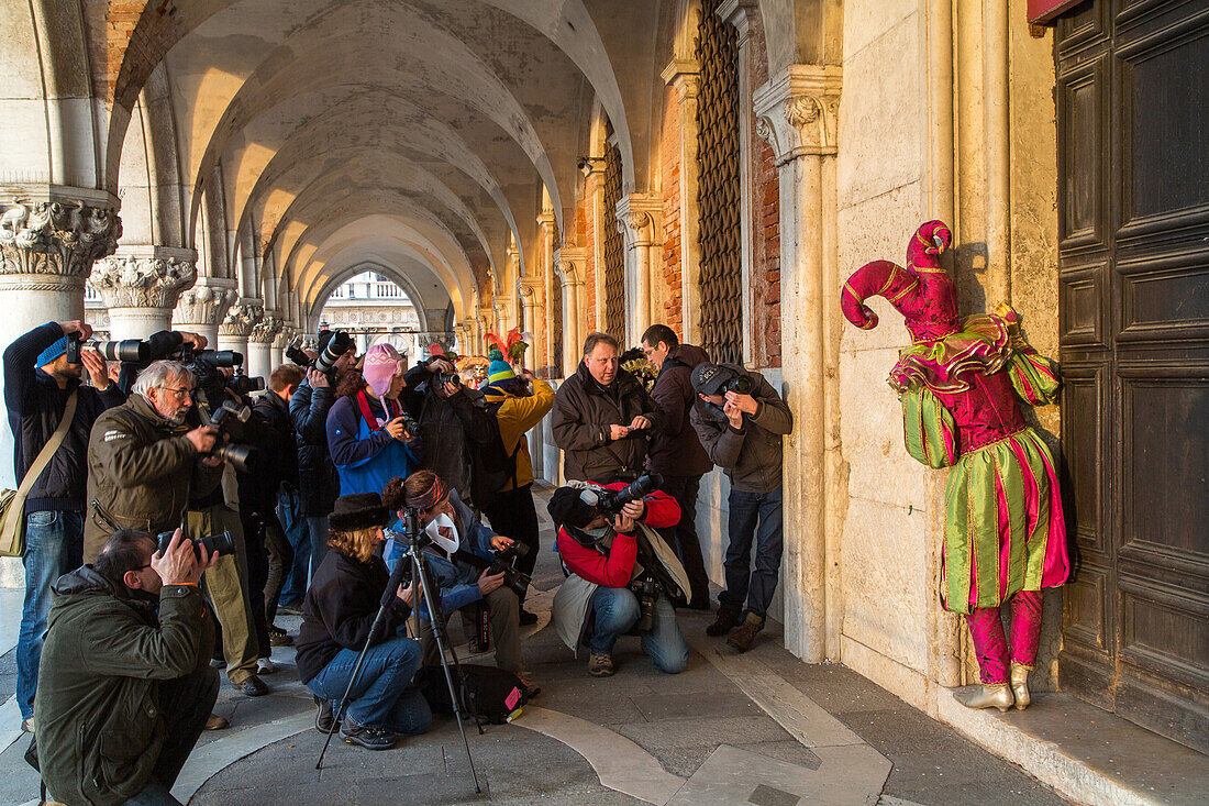 Venetian Carnival, tourism, masks, harlequin, jester, costume, posing, army of  photographers, arcade of Doge Palace, Venice, Italy