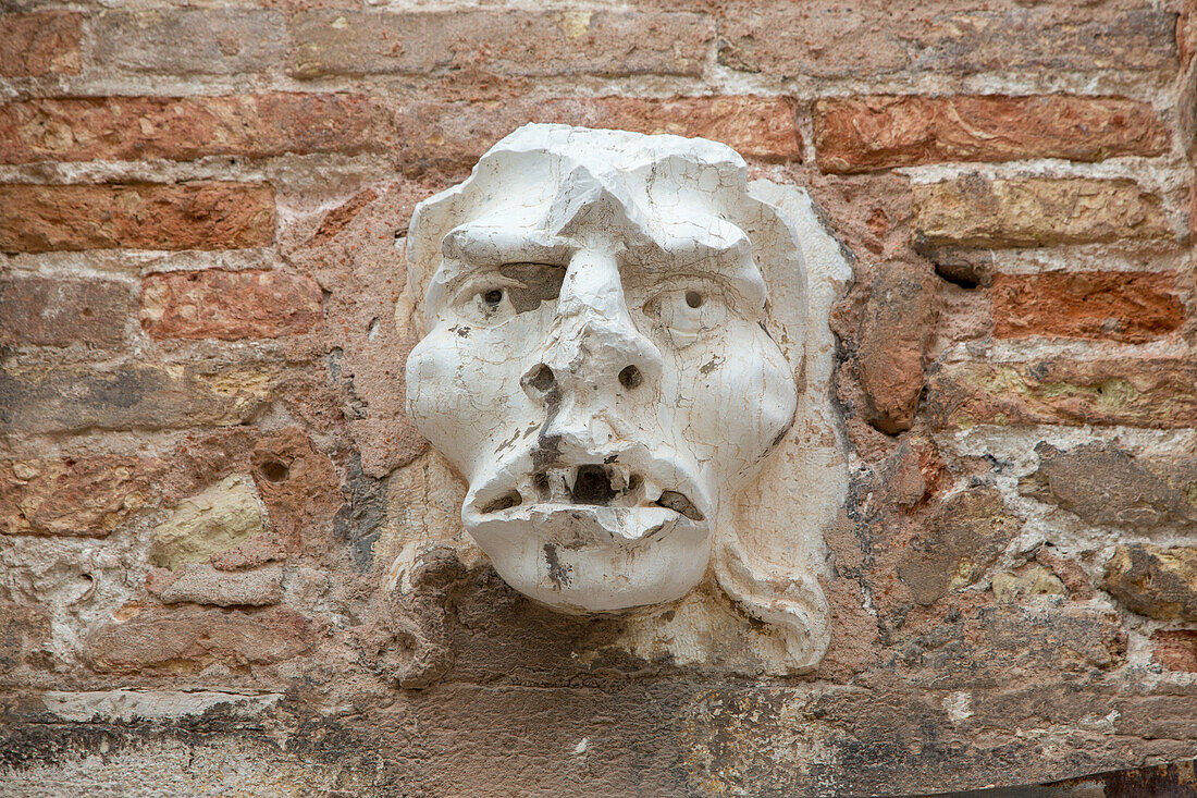 sculpture, stone relief of male head, open mouth and eyes, desperate, brickwall, Venice, Italy