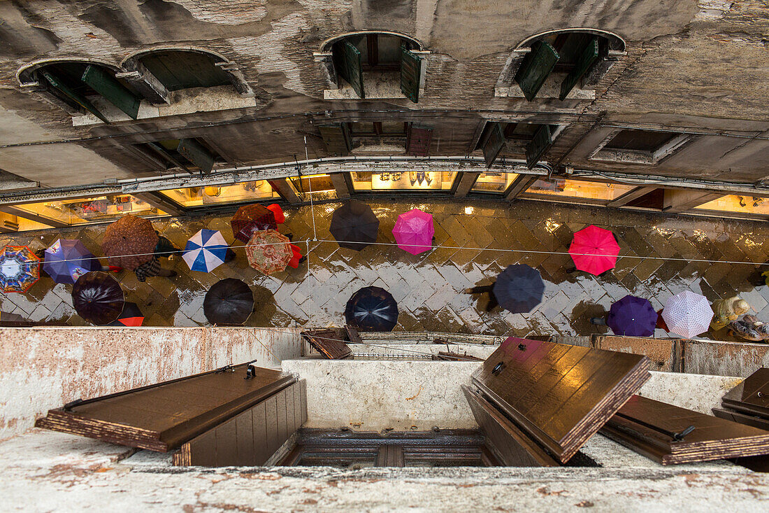 vertical view from upper floor down to pedestrians with umbrellas, Venice, Italy