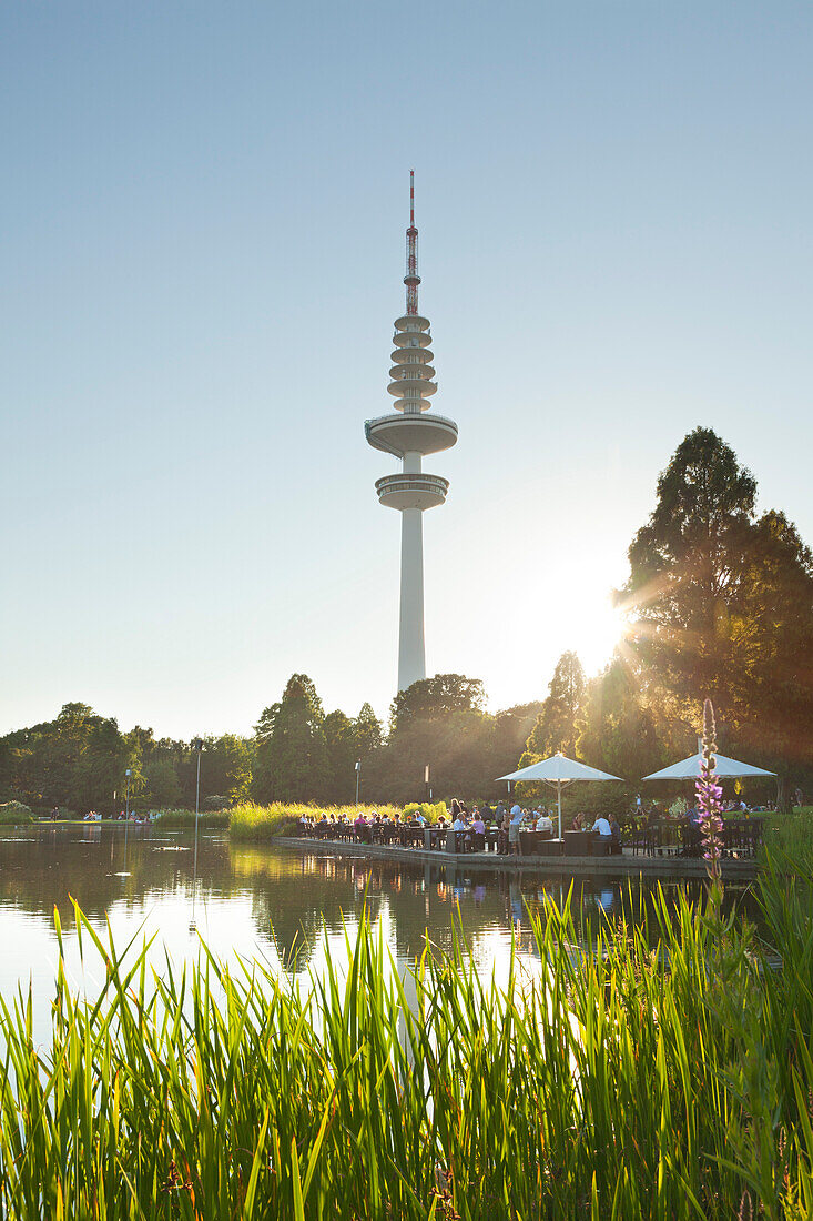 People sitting on the terrace of the Seepavillon snack bar at the park lake, television tower in the background, Planten un Blomen, Hamburg, Germany