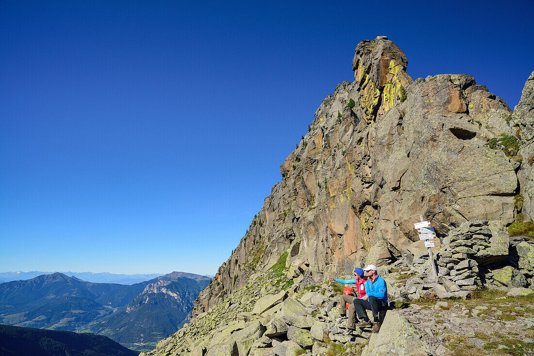 Zwei Wanderer sitzen unter Felsturm und blicken auf die Berge, Trans-Lagorai, Lagorai-Höhenweg, Lagorai, Dolomiten, UNESCO Welterbe Dolomiten, Trentino, Italien