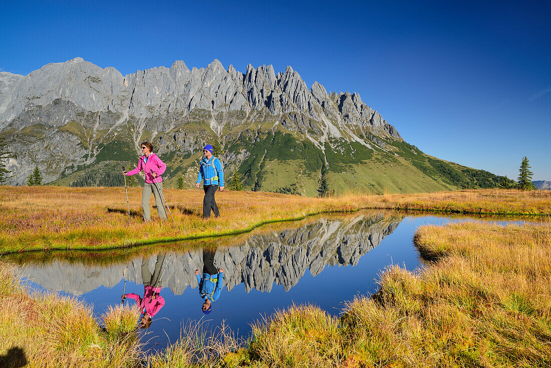 Man and woman hiking near a mountain lake with Mandlwand ridge at Hochkoenig in the background, Berchtesgaden range, Salzburg, Austria