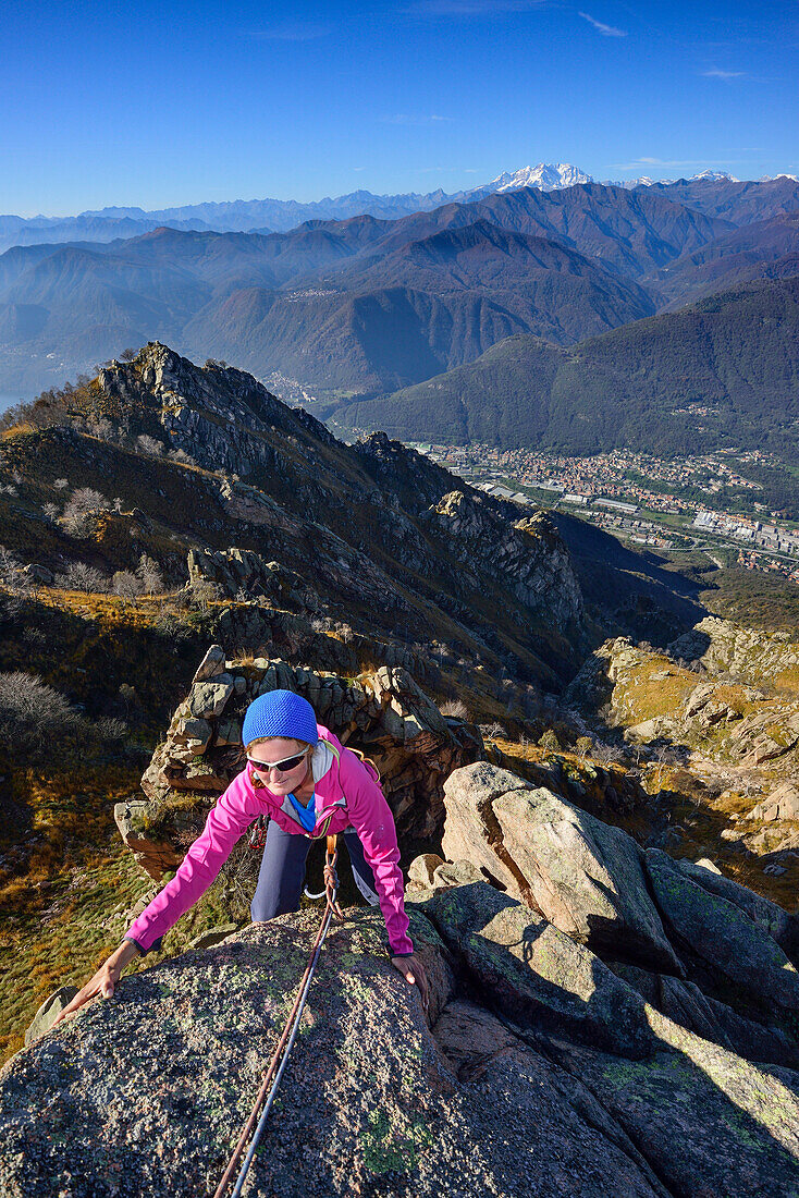 Frau klettert an roten Granitfelsen mit Blick auf Monte Rosa im Wallis, Mottarone, Piemont, Italien