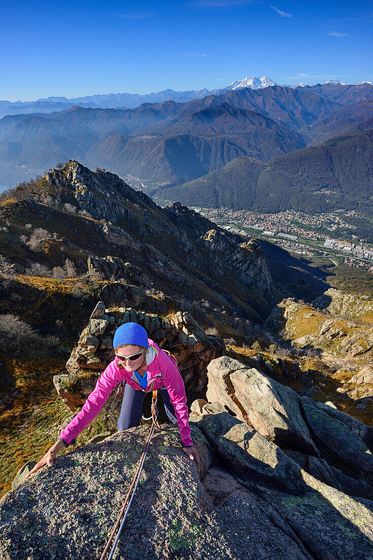 Woman climbing on red Granite rock with view to Monte Rosa in Valais, Mottarone, Piedmont, Italy