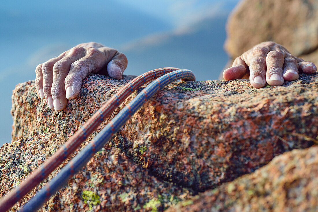 Zwei Hände einer Frau greifen beim Klettern über Felskante aus rotem Granit, Mottarone, Piemont, Italien