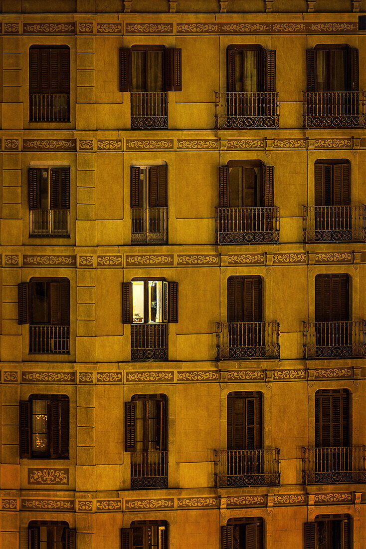 A single apartment light shines through the dark facade of a downtown building.