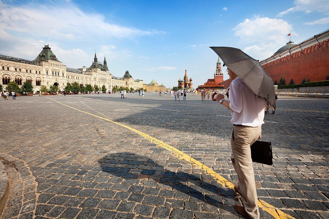 Moscow, Russia-July 20, 2010:An executive crosses the Red Square in Moscow with an umbrella shielding the intense heat of July and a little rain.