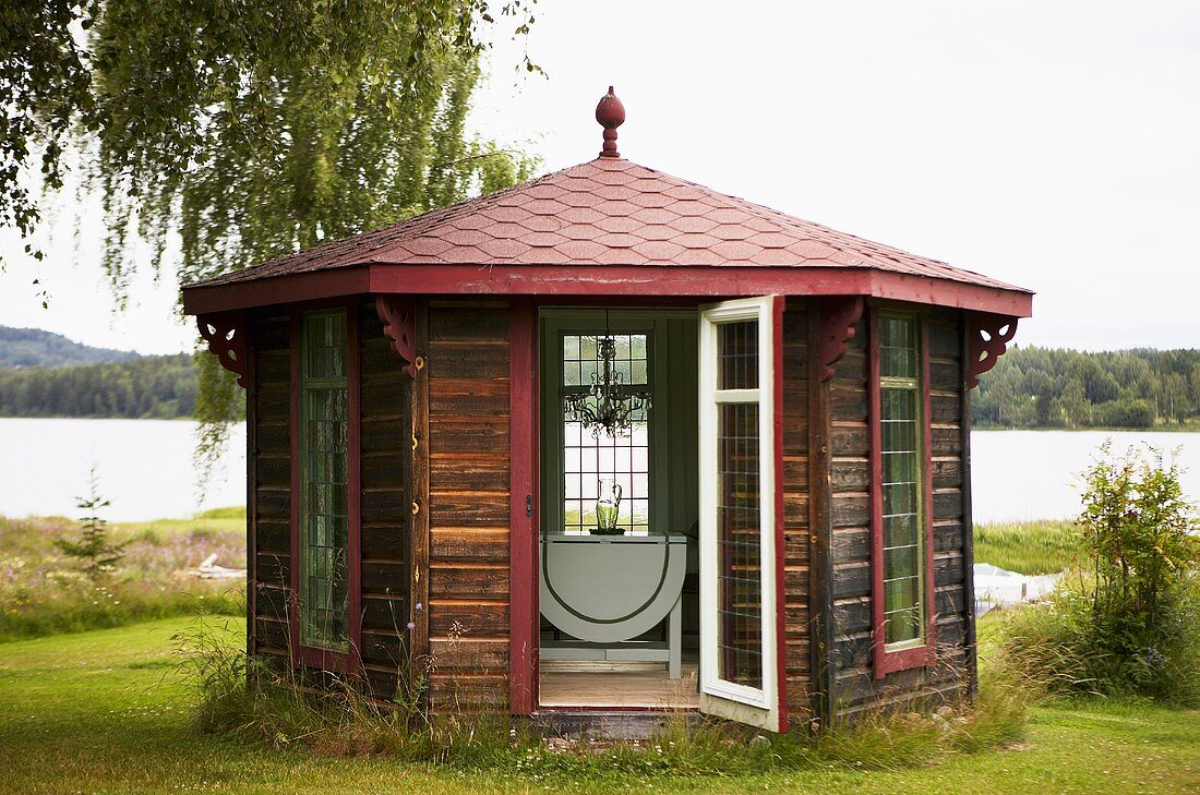 A gazebo with a red roof on the bank of a lake