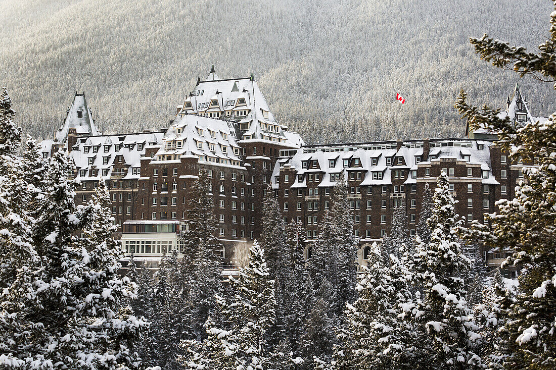 'Snow covered Banff Springs Hotel with snow covered trees and a Canadian flag; Banff, Alberta, Canada'