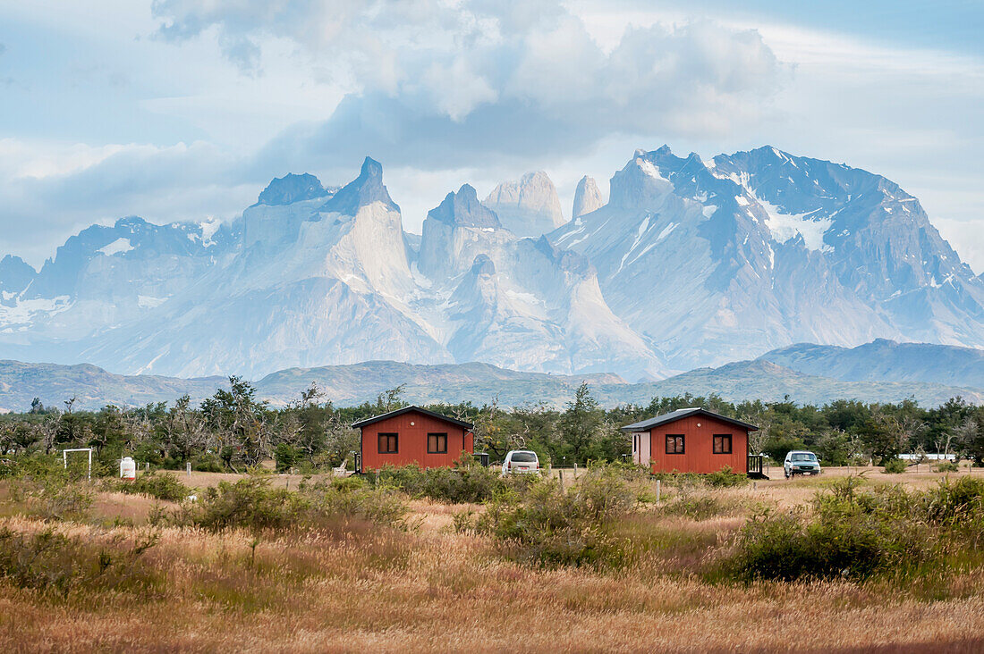 'Two small red cabins in front of rugged mountains; Torres del Pain, Chile'