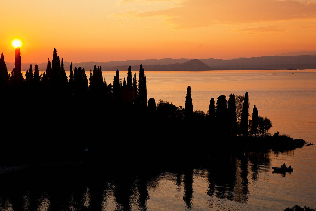 'Sunset glowing orange over Lake Garda with a silhouette of the shoreline; Tirol, Italy'