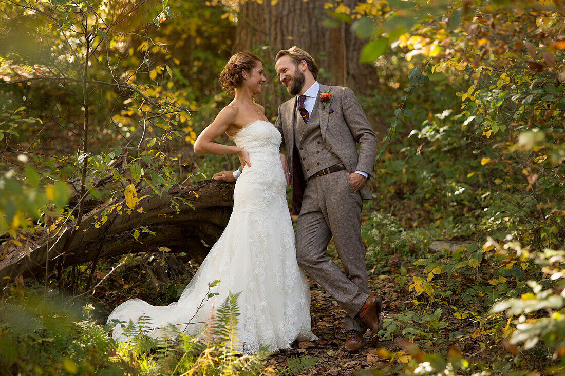 Bearded groom in grey suit and bride in wedding dress looking into each other?s eyes in the foliage of a forest
