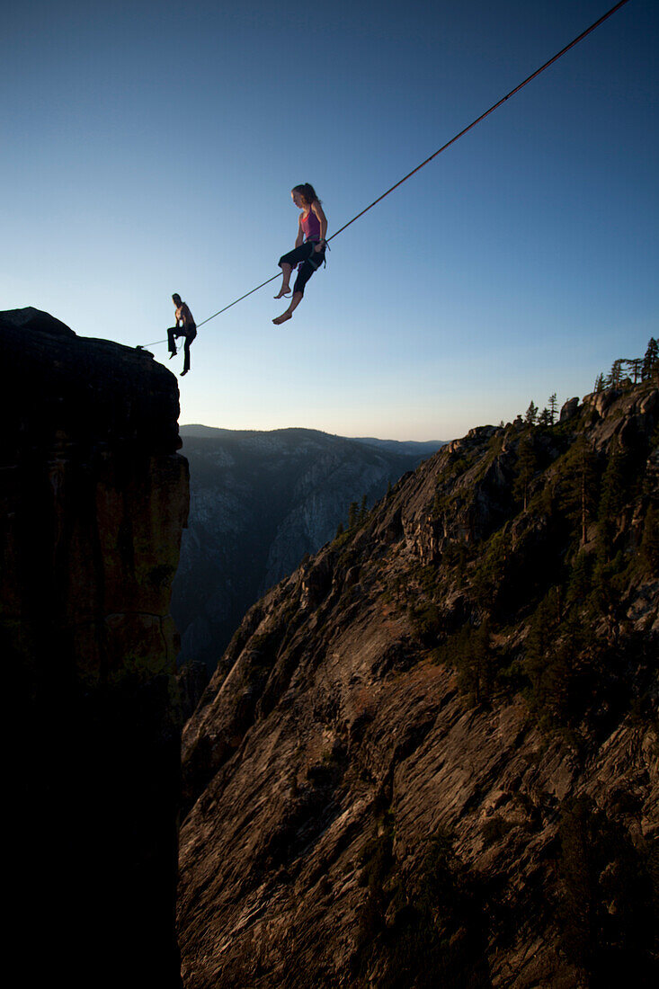 Female highliners simultaneously sitting on a highline above the Yosemite Valley floor at Taft Point