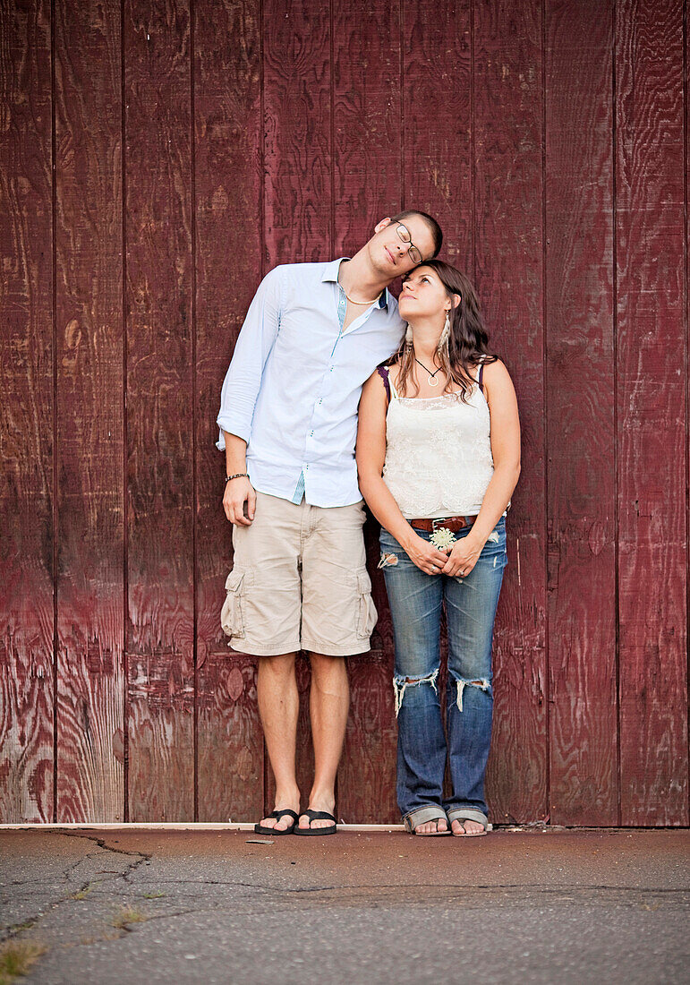 A young couple cuddles against the wall of a barn.