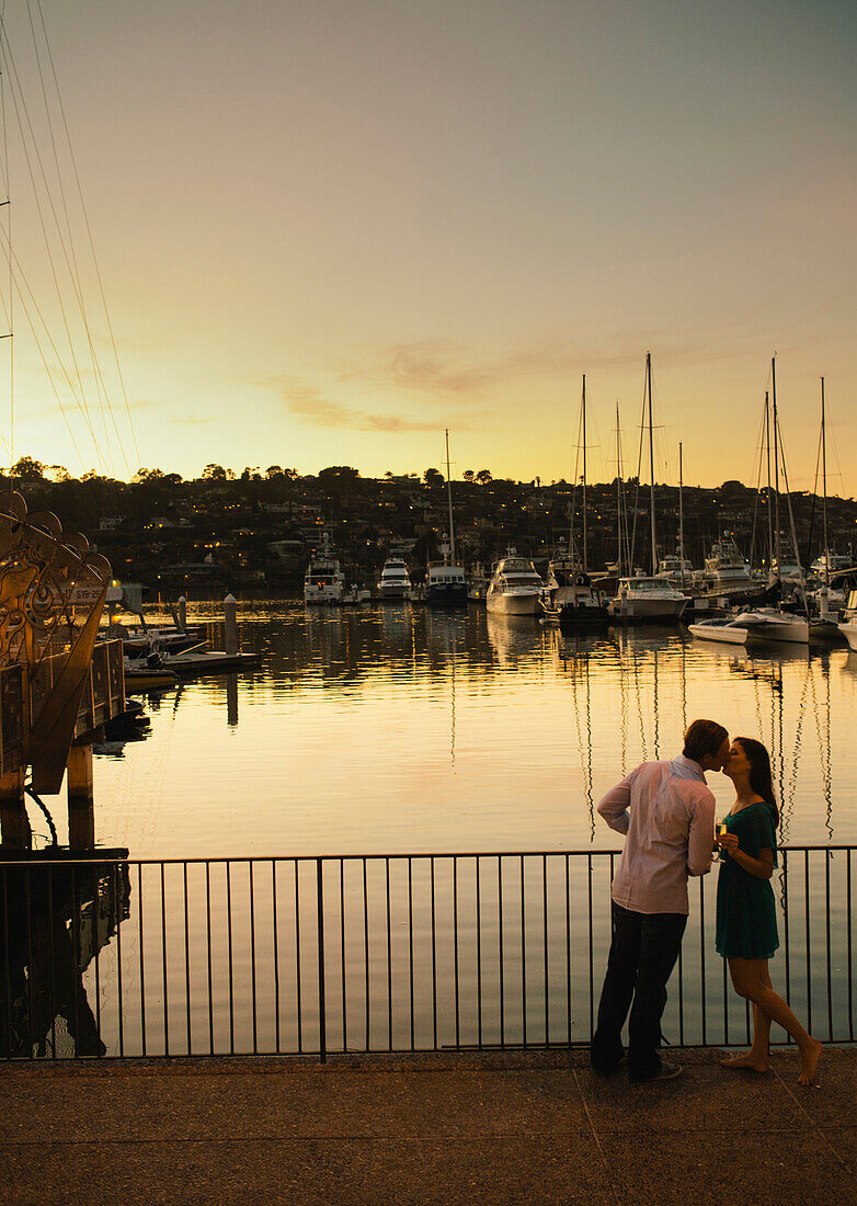 A young girl lip-locks with her male partner, stands by her side by the marina.
