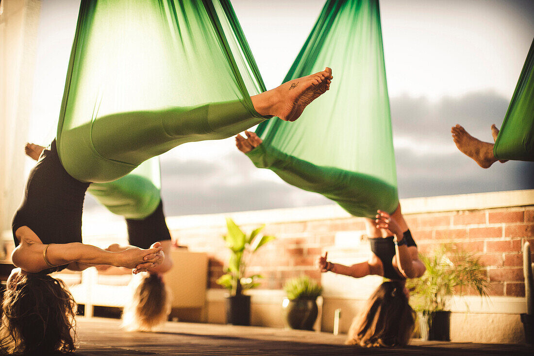 A group of women perform aerial yoga.